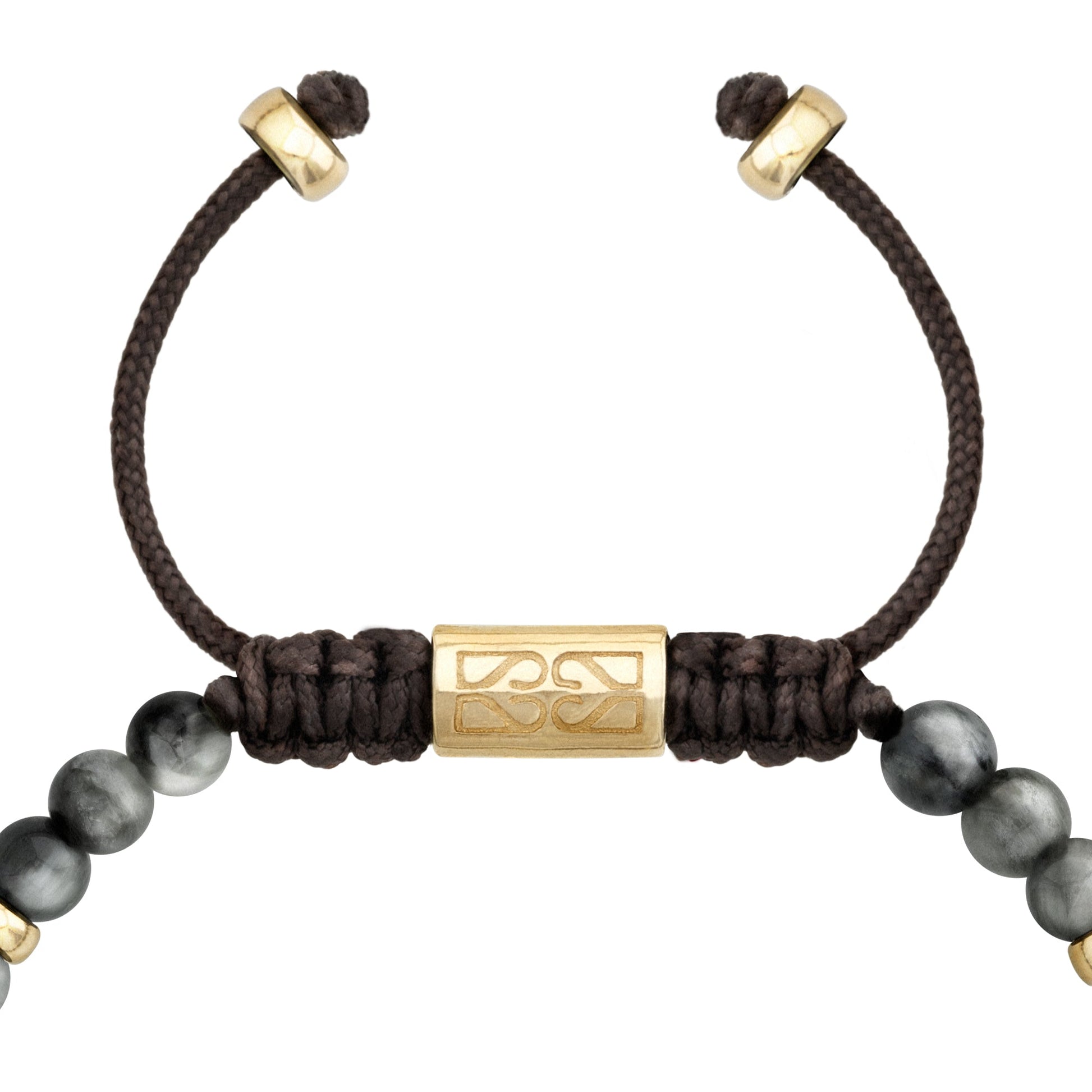Detalle del cierre ajustable de cordón negro con un cilindro dorado grabado, en una pulsera de cuentas grises y detalles dorados.